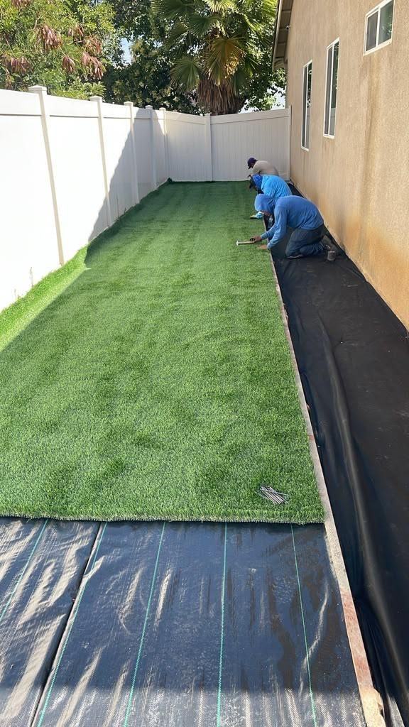 Crew installing artificial turf over weed barrier in a side yard
